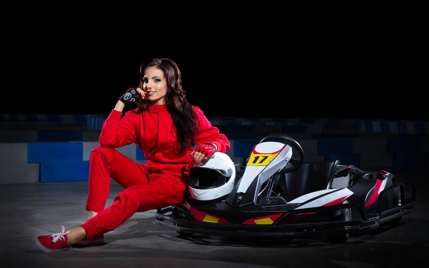Piros versenyruhás pilóta bukósisakokkal a gokart mellett